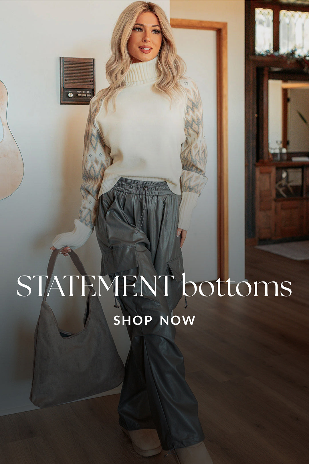 Woman wearing a white sweater and gray pants, holding a gray bag indoors.
