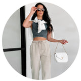 Model wearing taupe sweats with a charcoal brami and white sweatshirt tied around their shoulders. Links to New Arrivals. 