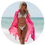 Model wearing a floral bikini with a pink cover up on the beach. Links to the swim collection.
